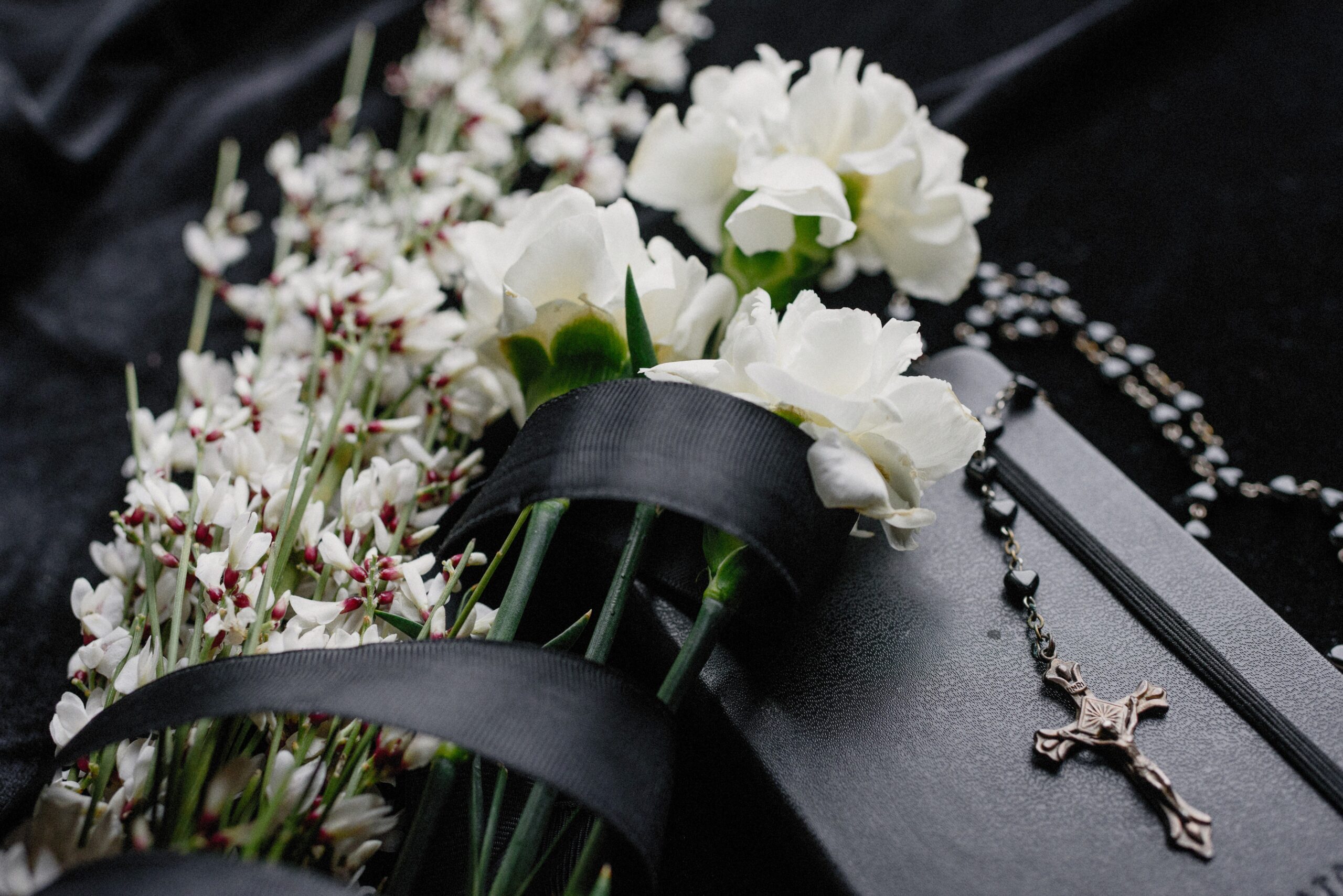 Vita begravningsblommor med svart begravningsband på kistan