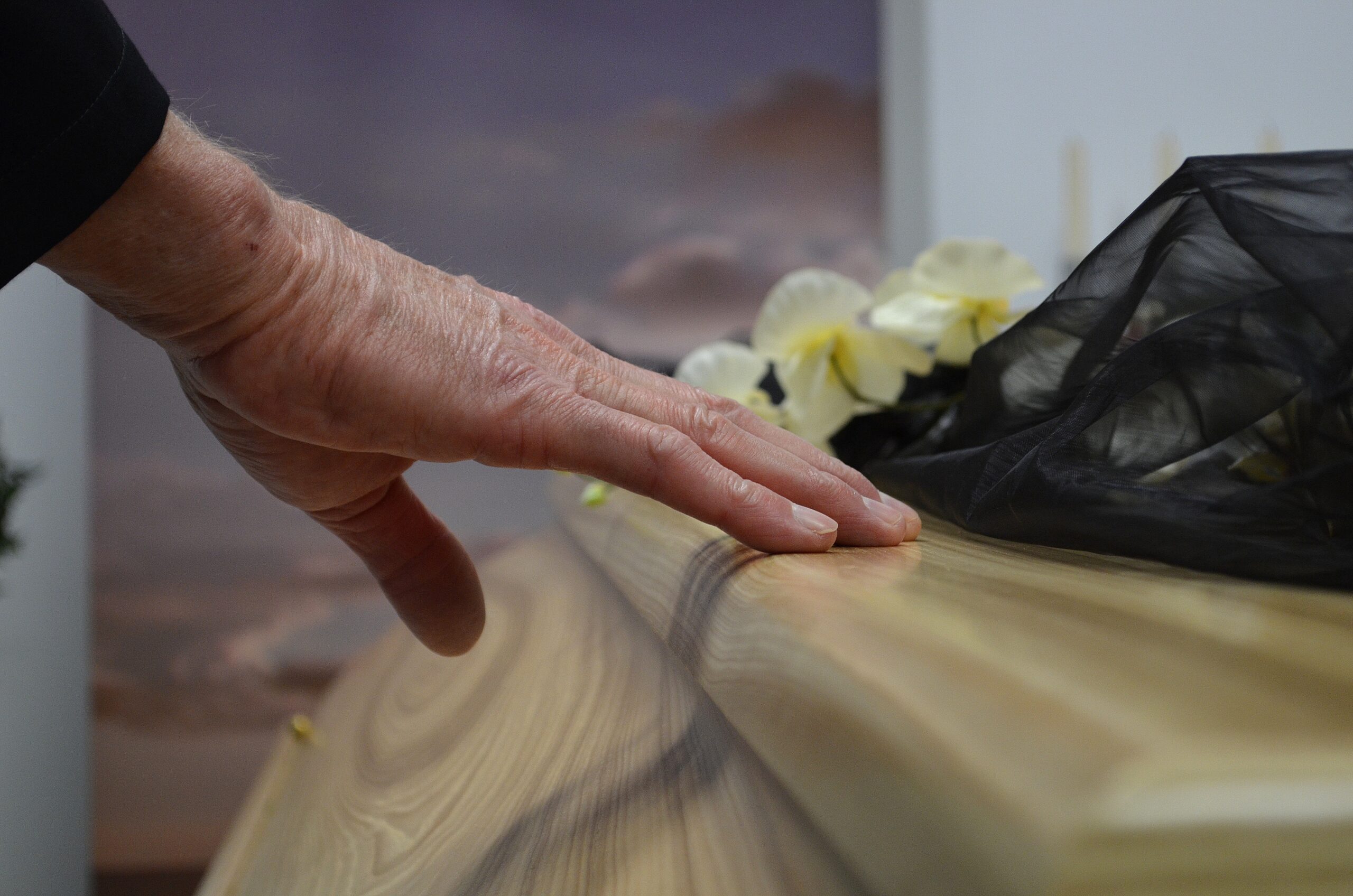 Begravning, hand på en kista med begravningsblommor